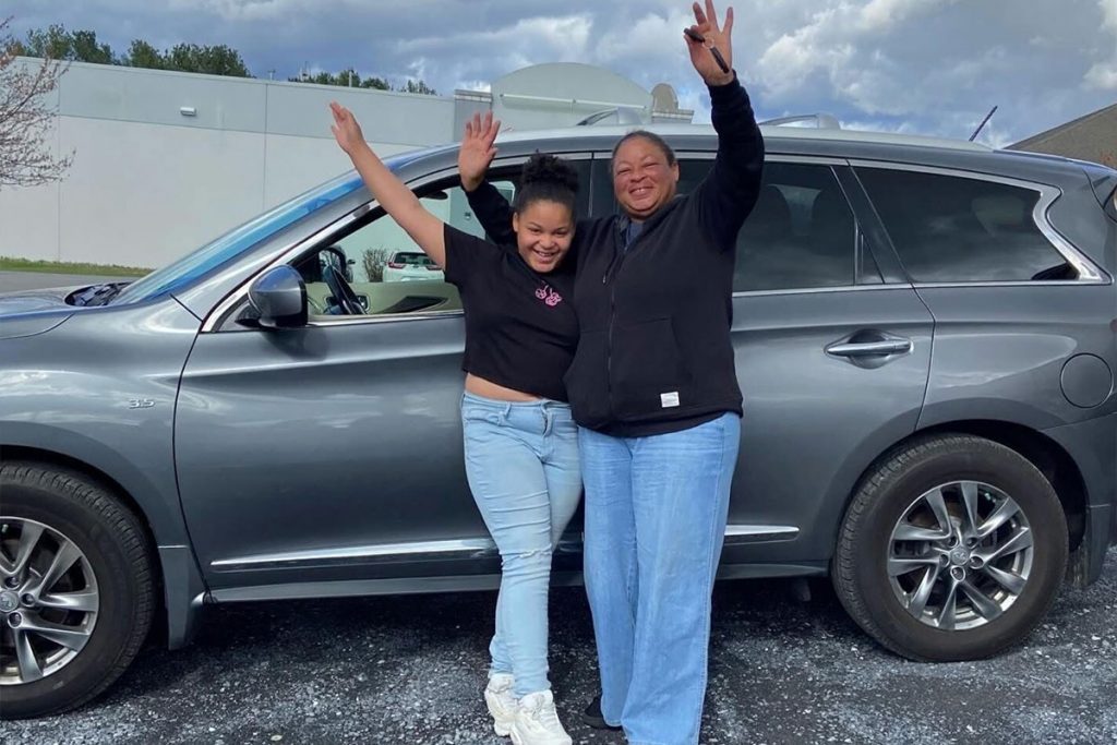 Image of a parent and a child in front of a car, celebrating.
