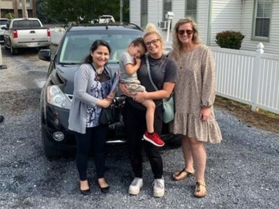 Image of four people in front of a donated car, celebrating new transportation.